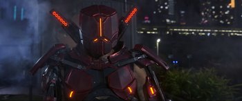 Movie still from “Blue Beetle” (2023), directed by Angel Manuel Soto – A man in a red suit is holding an arrow in his hand; Medium shot, Low angle
