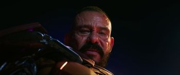 Movie still from “Blue Beetle” (2023), directed by Angel Manuel Soto – A person with a beard holding a gun; Close Up shot, Low angle