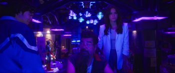 Movie still from “Blue Beetle” (2023), directed by Angel Manuel Soto – A man and a woman standing in a dark room; Medium shot, Over the shoulder angle