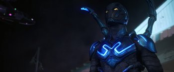 Movie still from “Blue Beetle” (2023), directed by Angel Manuel Soto – A person in a blue suit with glowing blue lights on it; Medium shot, Low angle
