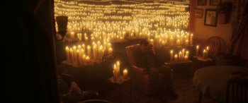 Movie still from “Blue Beetle” (2023), directed by Angel Manuel Soto – A man sitting in a chair surrounded by lit candles; Extreme Wide shot, High angle