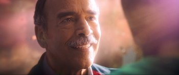 Movie still from “Blue Beetle” (2023), directed by Angel Manuel Soto – An older man with a mustache smiling for the camera; Extreme Close Up shot, Over the shoulder angle