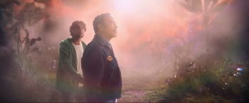 Movie still from “Blue Beetle” (2023), directed by Angel Manuel Soto – A man and a boy are standing in a field; Medium shot, Low angle