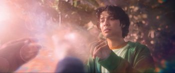 Movie still from “Blue Beetle” (2023), directed by Angel Manuel Soto – A young man holding something in his hand; Medium shot, Low angle