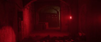 Movie still from “Blue Beetle” (2023), directed by Angel Manuel Soto – A dark room with red lighting and a large arch; Wide shot, Low angle