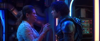 Movie still from “Blue Beetle” (2023), directed by Angel Manuel Soto – A woman talking to a young man in a room; Medium shot, Over the shoulder angle