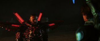 Movie still from “Blue Beetle” (2023), directed by Angel Manuel Soto – A man in a suit and glasses holding a sword in the dark; Medium shot, Low angle