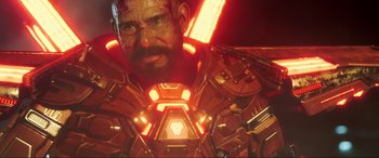 Movie still from “Blue Beetle” (2023), directed by Angel Manuel Soto – A man's face in a red and orange uniform; Close Up shot, Low angle