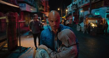 Movie still from “Blue Miracle” (2021), directed by Julio Quintana – A man with a bald head holding a baby in his arms; Medium shot, Over the shoulder angle