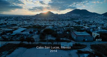 Movie still from “Blue Miracle” (2021), directed by Julio Quintana – An aerial view of a city at sunset with the sun setting; Extreme Wide shot, Overhead angle