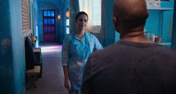 Movie still from “Blue Miracle” (2021), directed by Julio Quintana – A woman standing in front of a man in a blue room; Medium shot, Over the shoulder angle