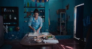 Movie still from “Blue Miracle” (2021), directed by Julio Quintana – A woman in an apron is preparing food on a table; Wide shot, Low angle