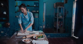 Movie still from “Blue Miracle” (2021), directed by Julio Quintana – A woman in a blue apron is making a pizza; Medium shot, Over the shoulder angle
