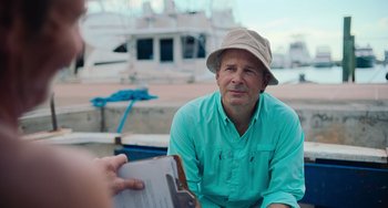 Movie still from “Blue Miracle” (2021), directed by Julio Quintana – A man wearing a hat sitting next to another man holding a clipboard; Medium shot, Over the shoulder angle