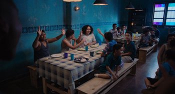 Movie still from “Blue Miracle” (2021), directed by Julio Quintana – A group of people sitting at a table with food; Wide shot, High angle