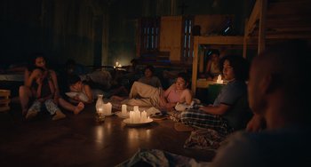 Movie still from “Blue Miracle” (2021), directed by Julio Quintana – A group of people sitting on the floor with candles; Wide shot, High angle