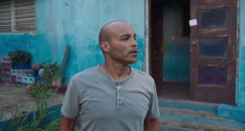 Movie still from “Blue Miracle” (2021), directed by Julio Quintana – A man with a shaved head standing in front of a blue wall; Medium shot, Low angle
