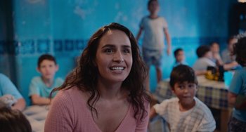 Movie still from “Blue Miracle” (2021), directed by Julio Quintana – A woman smiles in front of a blue wall; Close Up shot, Over the shoulder angle