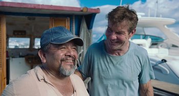 Movie still from “Blue Miracle” (2021), directed by Julio Quintana – Two men are laughing together on a boat; Medium shot, Over the shoulder angle