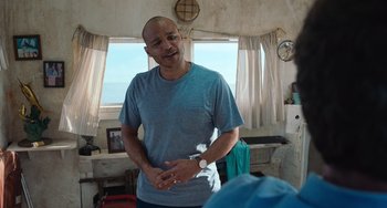 Movie still from “Blue Miracle” (2021), directed by Julio Quintana – A man standing in front of a window in a room; Medium shot, Over the shoulder angle