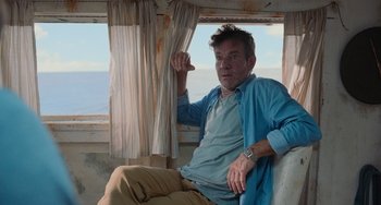 Movie still from “Blue Miracle” (2021), directed by Julio Quintana – A man sitting on a chair in front of a window; Medium shot, Low angle