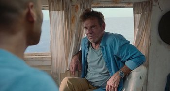 Movie still from “Blue Miracle” (2021), directed by Julio Quintana – A man sitting on a chair in front of a window; Medium shot, Over the shoulder angle
