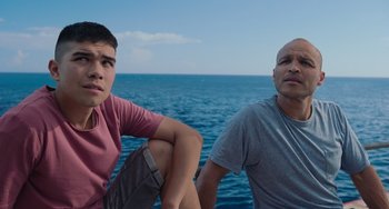 Movie still from “Blue Miracle” (2021), directed by Julio Quintana – Two men sitting on a boat in front of the ocean; Medium shot, High angle