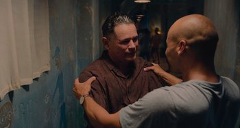 Movie still from “Blue Miracle” (2021), directed by Julio Quintana – A man is being hugged by another man in a hallway; Medium shot, Over the shoulder angle