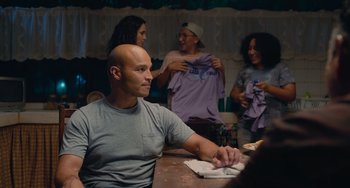 Movie still from “Blue Miracle” (2021), directed by Julio Quintana – A man sitting at a table in front of a group of people; Medium shot, Over the shoulder angle