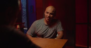 Movie still from “Blue Miracle” (2021), directed by Julio Quintana – A man sitting at a wooden table in front of a window; Medium shot, Over the shoulder angle