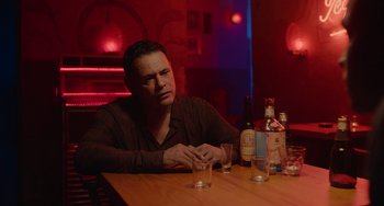 Movie still from “Blue Miracle” (2021), directed by Julio Quintana – A man sitting at a table in front of a glass of water; Medium shot, Low angle
