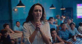 Movie still from “Blue Miracle” (2021), directed by Julio Quintana – A woman with her hands clasped in front of a crowd; Close Up shot, Over the shoulder angle