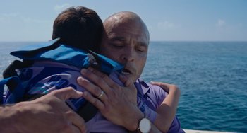 Movie still from “Blue Miracle” (2021), directed by Julio Quintana – A man holding a child in his arms near the ocean; Close Up shot, Over the shoulder angle