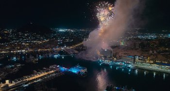 Movie still from “Blue Miracle” (2021), directed by Julio Quintana – Fireworks are being set off in the night sky over a harbor; Extreme Wide shot, High angle