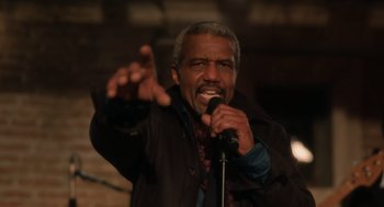 Movie still from “Book Club: The Next Chapter” (2023), directed by Bill Holderman – A man with a beard is holding a microphone; Medium shot, Low angle