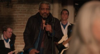 Movie still from “Book Club: The Next Chapter” (2023), directed by Bill Holderman – An older man holding a microphone while standing in front of a man playing a guitar; Medium shot, Over the shoulder angle