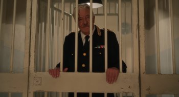 Movie still from “Book Club: The Next Chapter” (2023), directed by Bill Holderman – An old man in a uniform standing behind bars in a jail cell; Medium shot, Low angle