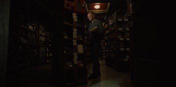 Movie still from “Books of Blood” (2020), directed by Brannon Braga – A man is standing in a book store holding a book; Medium shot, Low angle