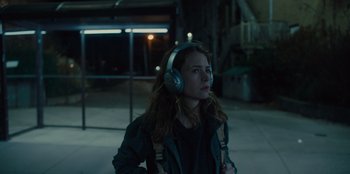 Movie still from “Books of Blood” (2020), directed by Brannon Braga – A woman wearing headphones while standing in a parking lot; Medium shot, Over the shoulder angle