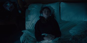 Movie still from “Books of Blood” (2020), directed by Brannon Braga – A woman laying in a bed wearing headphones; Medium shot, Overhead angle