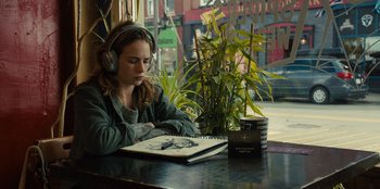 Movie still from “Books of Blood” (2020), directed by Brannon Braga – A woman sitting at a table with a book and headphones; Medium shot, Over the shoulder angle