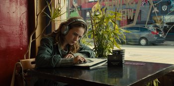 Movie still from “Books of Blood” (2020), directed by Brannon Braga – A woman sitting in front of a laptop computer on top of a table; Medium shot, Over the shoulder angle