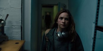 Movie still from “Books of Blood” (2020), directed by Brannon Braga – A woman with headphones in a hallway with a man in the background; Medium shot, Over the shoulder angle
