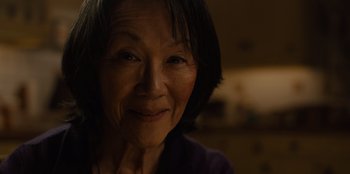 Movie still from “Books of Blood” (2020), directed by Brannon Braga – An older asian woman smiling for the camera; Extreme Close Up shot, Over the shoulder angle