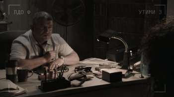 Movie still from “Borat Subsequent Moviefilm” (2020), directed by Jason Woliner – A man sitting at a table with a lot of electronics; Medium shot, Low angle