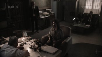Movie still from “Borat Subsequent Moviefilm” (2020), directed by Jason Woliner – A man sitting in a chair in front of a desk; Wide shot, Over the shoulder angle