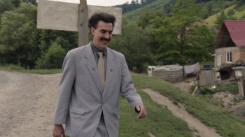Movie still from “Borat Subsequent Moviefilm” (2020), directed by Jason Woliner – A man wearing a suit and tie walking on a dirt road; Medium shot, Over the shoulder angle
