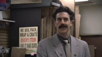 Movie still from “Borat Subsequent Moviefilm” (2020), directed by Jason Woliner – A man in a suit and tie standing in a store; Close Up shot, Over the shoulder angle