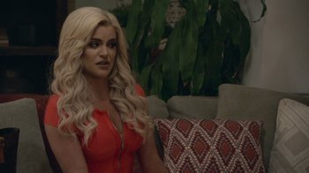 Movie still from “Borat Subsequent Moviefilm” (2020), directed by Jason Woliner – A woman sitting on a couch in a living room; Close Up shot, Over the shoulder angle