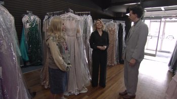 Movie still from “Borat Subsequent Moviefilm” (2020), directed by Jason Woliner – A woman standing next to two men in a dress store; Wide shot, Over the shoulder angle